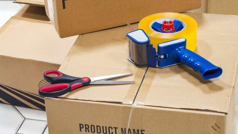 A roll of tape and scissors on top of a moving box.