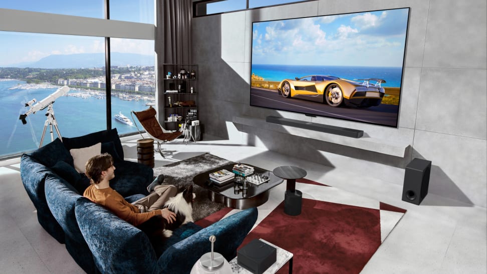 An upscale living room in which the LG M4 wireless OLED TV hangs on the wall in front of a happy viewer and  dog sitting on a couch