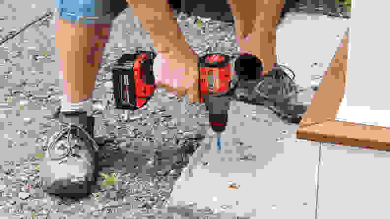 A person using the Milwaukee M18 Cordless Hammer Drill to drill a concrete step outdoors.