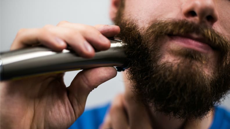 Close-up: a person trims their beard with a strainless-steel electric trimmer.