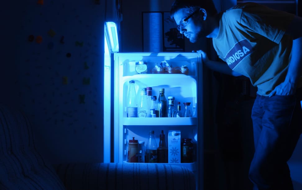 A man looking inside a refrigerator at night