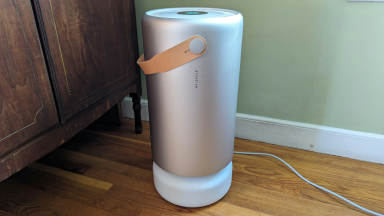 A silver Molekule air purifier is shown in a home on top of wooden floor.