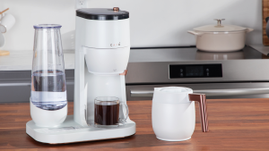 A white, GE Café Specialty Grind and Brew Coffee Maker in a kitchen setting, with a cup of coffee inside the machine.
