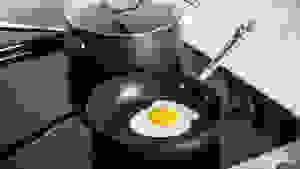 一个完美的煎蛋内，在一个不克服的平底锅里面，在它后面的一个不舔锅，既坐在炉灶上。