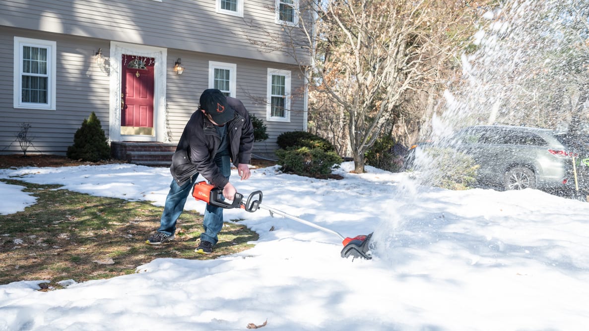 A man using an electric snow shovel to clear snow in front of his house.