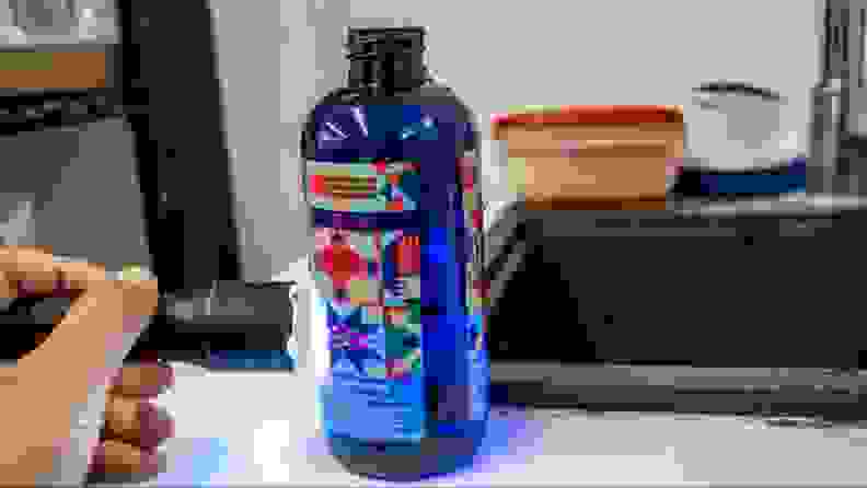 A person holding a flashlight and shining it into a dark blue bottle of Truly Free Space Freshener with a colorful graphic label.