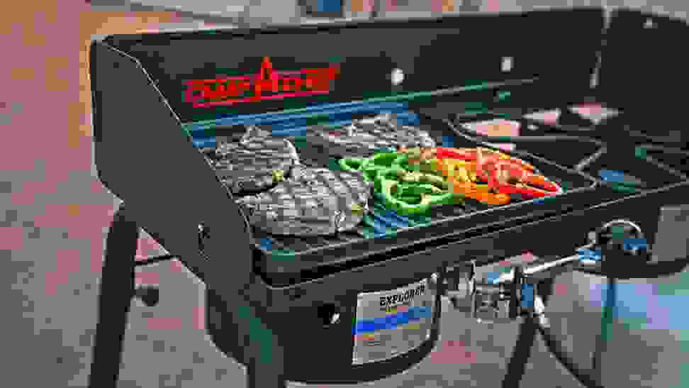 Protein and green and red peppers cook on a black Camp Chef portable grill.