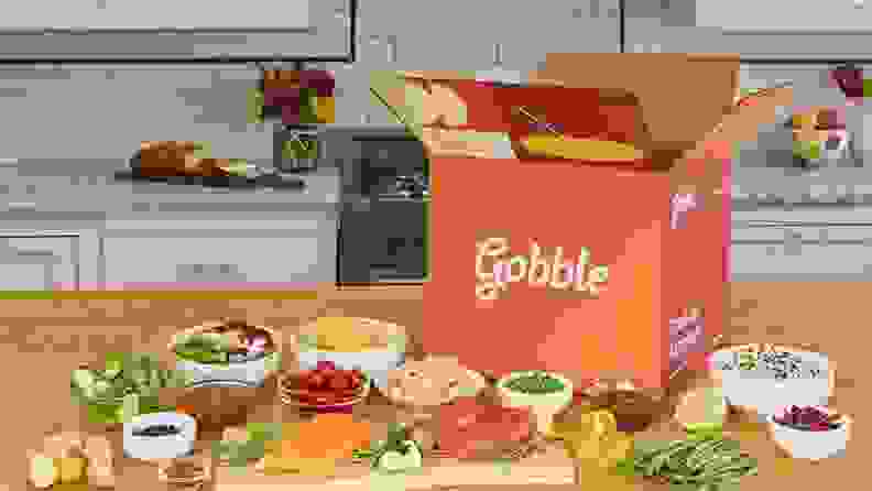 A Gobble meal kit box surrounded by fresh produce and other ingredients on a wooden kitchen countertop.