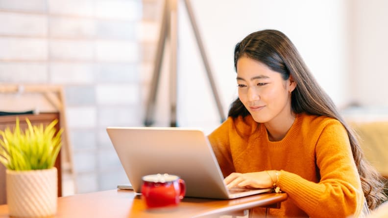 A woman in an orange sweater typing on her laptop.