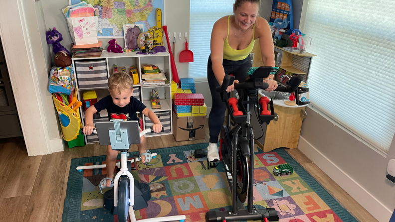 A child and person each ride a stationary fitness bike side by side
