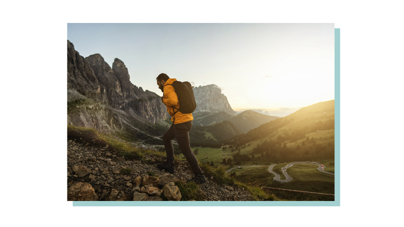A person hiking up a mountain trail with a panoramic sunset view.