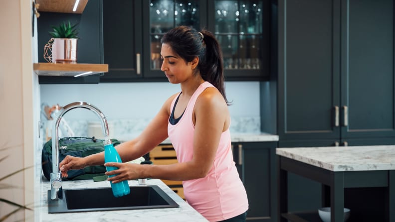 A woman filling up her water bottle at the kitchen sink.