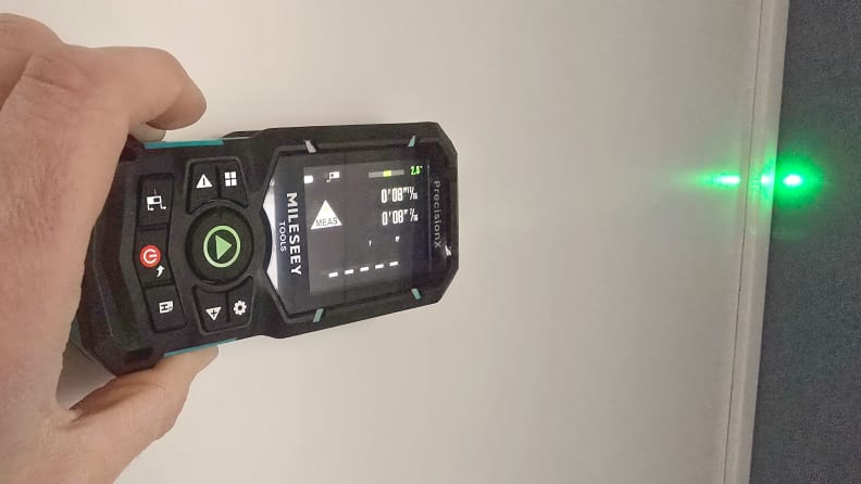 A hand holds a laser level with a green beam