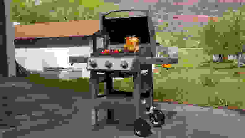 The Weber Spirit II E-310 open, showing a whole rotisserie chicken and vegetables cooking, in a backyard.