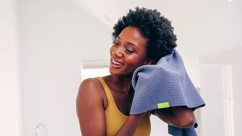 A person holding the blue Aquis Waffle Luxe Hair Towel up to their hair to dry it.
