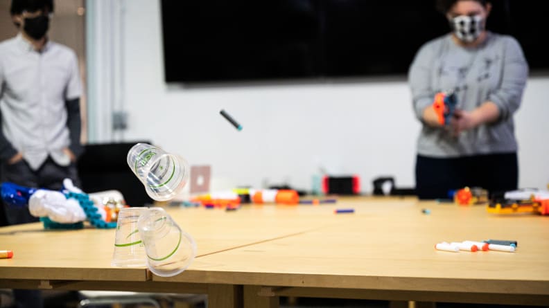 A person aiming a Nerf gun at a target of plastic cups