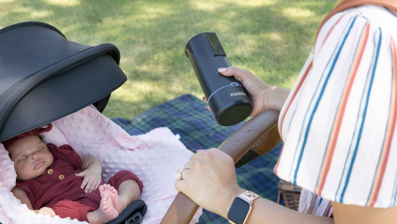 A mom pushing a stroller holding the Keddle milk warmer.