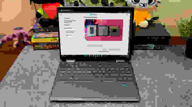 An open laptop on a desk, with books and tchotchkes in the background