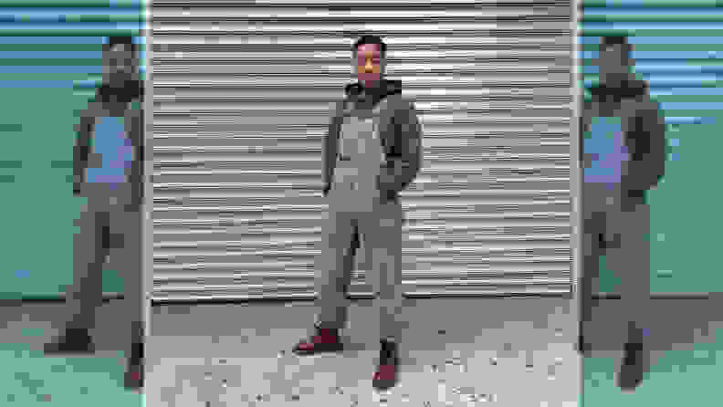A person wearing overalls, red boots, and a gray hoodie, standing in front of a metal background.