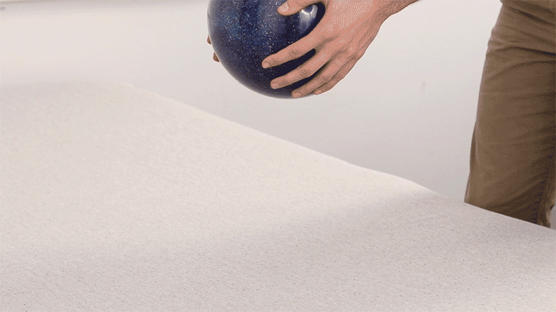 A person dropping a bowling ball onto a mattress.