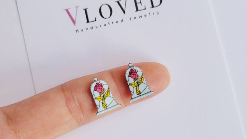 A finger holding two earrings featuring roses