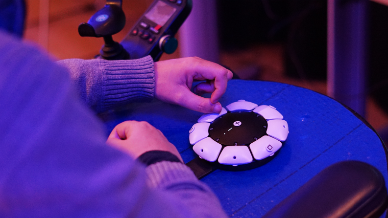 Person using hand to operate the joystick on the PS5 Access Controller while sitting in wheelchair.