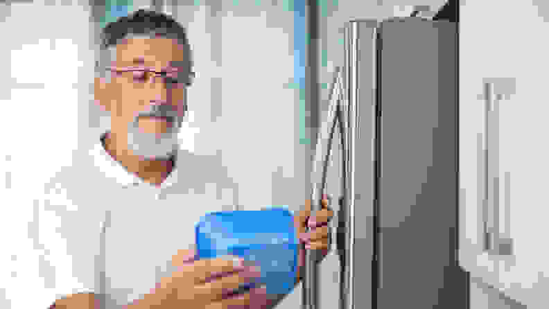 A man stands in front of his fridge, examining a package of frozen food. The fridge is in profile, and you can see it sticking out about six inches beyond the rest of his cabinetry.