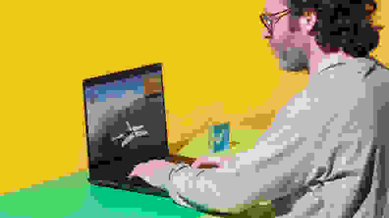 A person sitting at a two-tone green and yellow desk while typing on the Alienware m16 R2 gaming laptop.
