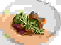 一个白色和橙色的盘子，里面装满了炖牛尾，上面放着微绿色蔬菜。