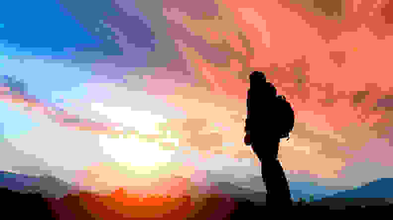 An image of a person staring at a sunset while hiking.