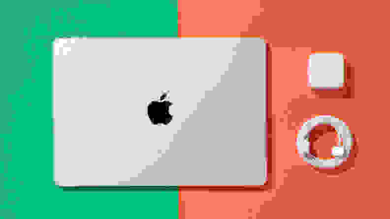 The Apple MacBook Air 13 M3 with its power brick and USB-C charging cable on a green and orange background.