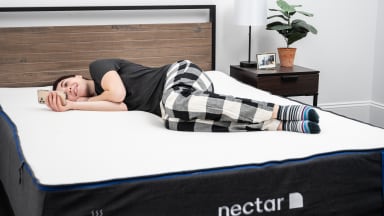 A woman reads her phone on the Nectar mattress