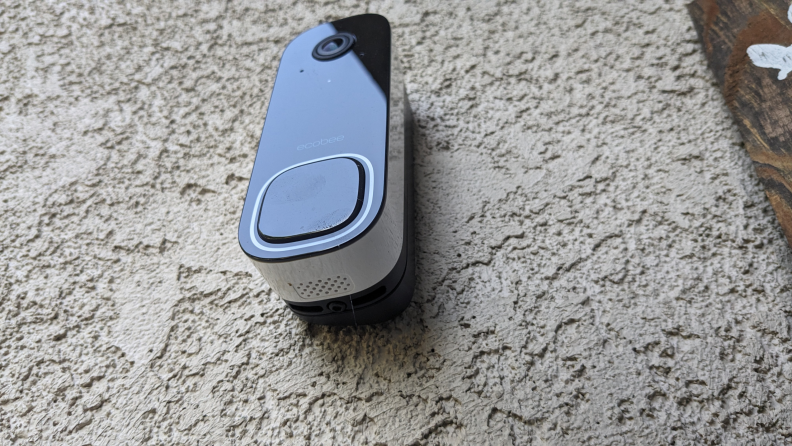 The Ecobee Smart Doorbell Camera photographed from a bottom angle showing off the doorbell press button on the outside of a home