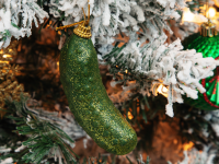 A close-up of a Christmas pickle ornament on a flocked Christmas tree.