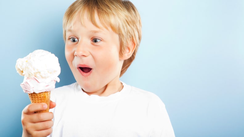 A boy holding an ice cream cone and very excited to eat it.