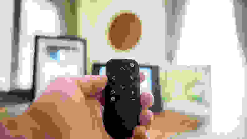 A hand points a small black remote at three digital picture frames sitting on a table.