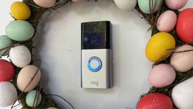 The Ring Battery Doorbell Plus hangs on a white front door surrounded by an Easter egg wreath
