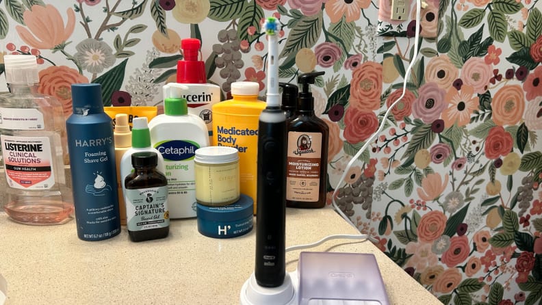 A black toothbrush sits on a bathroom counter with cosmetics in the background