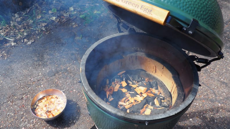 A manado grill is open to reveal hot coals and wood chips within.