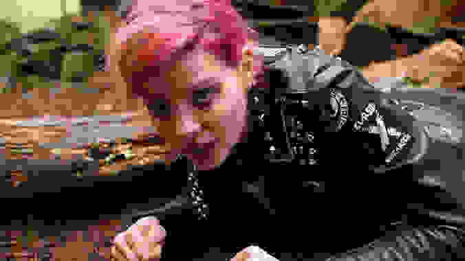 A woman with pink hair and in a black leather jacket on the ground, in a scene from