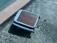 A blue square pool robot sits on top of the water