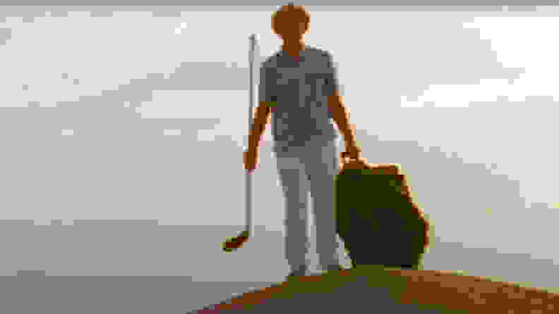 A man walking in the desert with a bag and a hockey stick