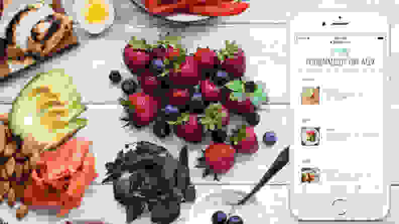 Nibs of chocolate, berries, and sliced avocado on table next to phone with PlateJoy app on it.