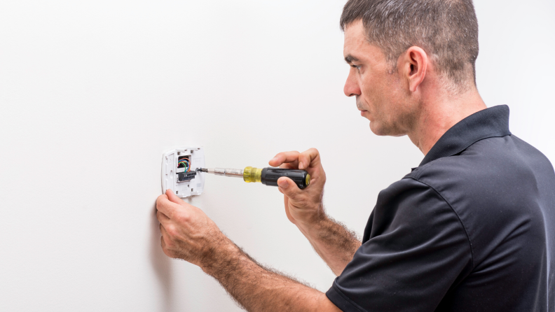 Man installing a smart thermostat with a screwdriver