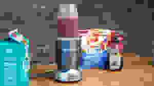 营养不良的个人搅拌机装满浆果冰沙坐在其成分旁边的柜台上。