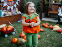 Child smiling outdoors while dressed in jack-o'-lantern Halloween costume.