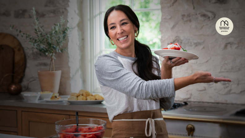TV chef Joanna Gaines, smiling, holds up a plate of strawberry dessert.