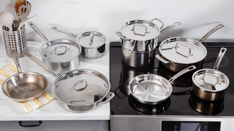 Several stainless steel pots and pans laid out on a cooktop and countertop