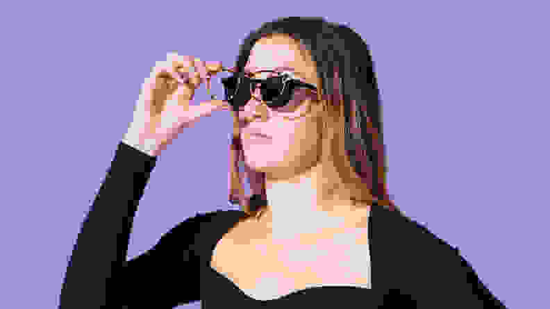 Woman wearing black shirt and pair of eyeglasses in front of purple background