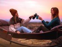 Two friends sitting on their camping hammock during a trip.